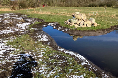 Gewässer und Steinhaufen auf einem Acker mit etwas Schnee bedeckt